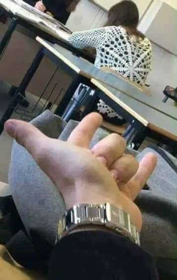 First person view of a hand with fingers bent into a strange shape in a classroom.