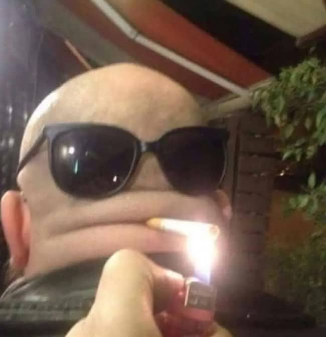 Bald head wearing sunglasses on the back, posed like a face lighting a cigarette.