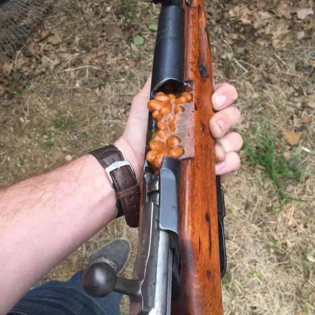 Rifle with baked beans stuffed into its open chamber, held in a first person view.