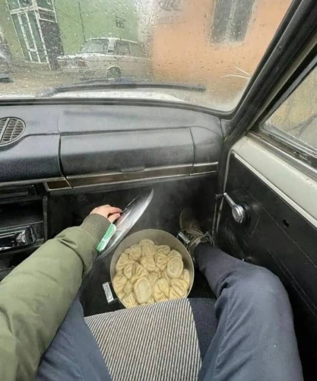 Pot of steaming dumplings sitting on a car floor next to a passenger's feet.