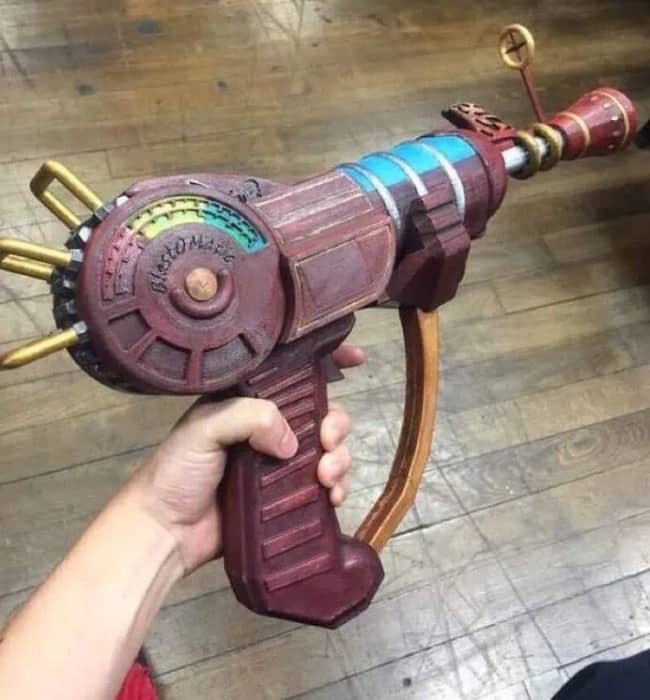 Hand holding a detailed replica video game ray gun above a scuffed wooden floor.