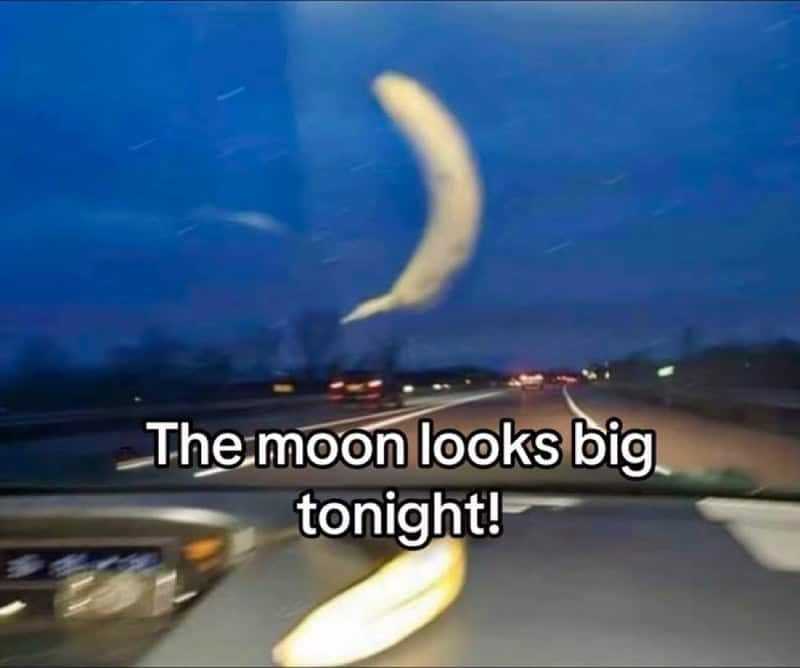 A banana stuck to a car windshield at dusk looks like a giant crescent moon.