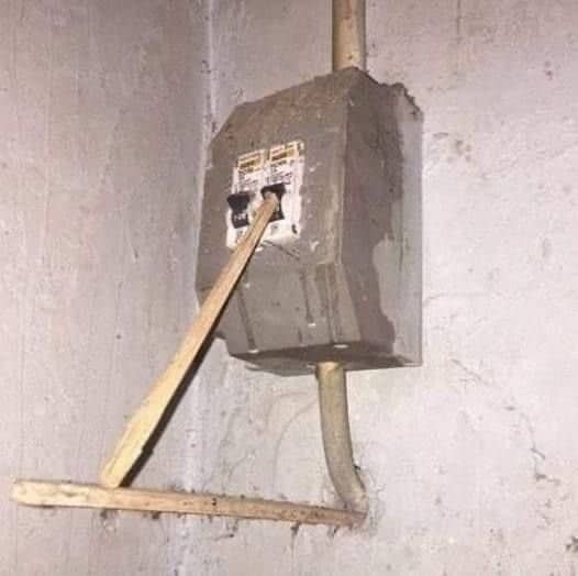 Electrical breaker box hanging off a concrete wall propped up by a wooden stick