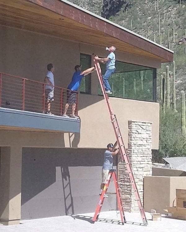 Extension ladder running from a balcony to a roof with a second ladder propped beneath it