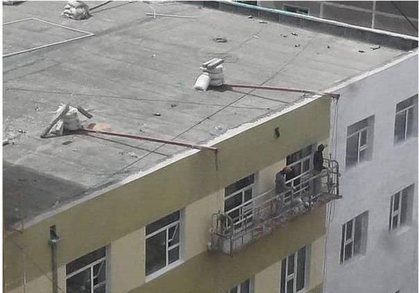 Suspended work platform on a building side with its roof anchors weighted by loose rubble