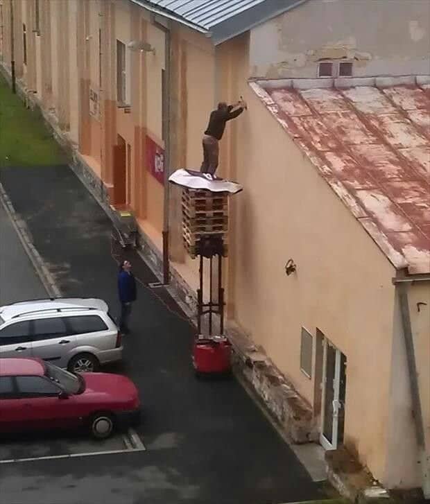 Man standing on a stack of pallets lifted high by a warehouse pallet jack