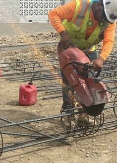 Construction worker cutting rebar with a handheld saw beside a red fuel can on site