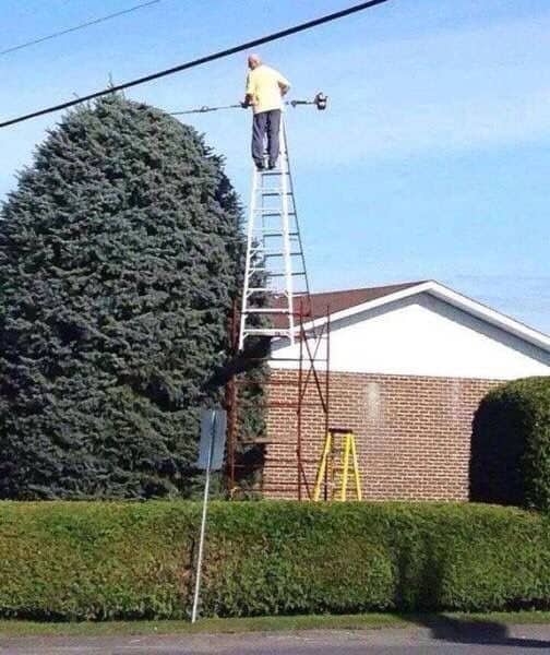 Man standing at the top of a tall extension ladder reaching toward an overhead power line