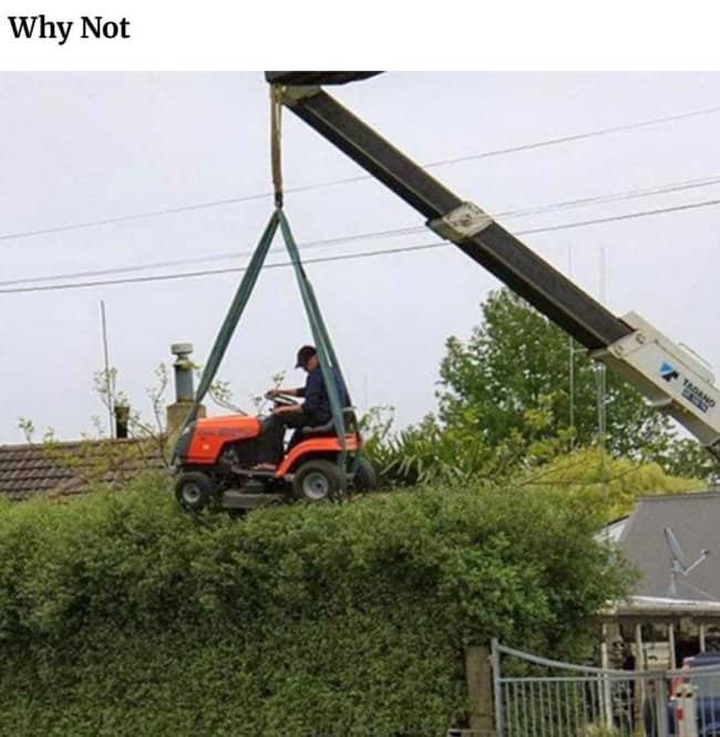 Crane lifting a riding mower over a hedge with a man still in the seat