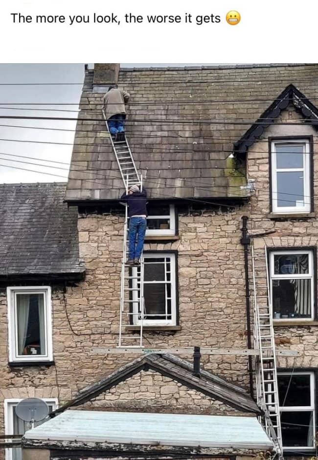 Two ladders stacked up a house facade with one man on the roof and another climbing
