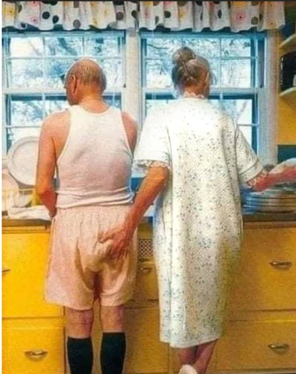 Elderly couple standing together in kitchen where wife grabs husband's rear in seniors memes.