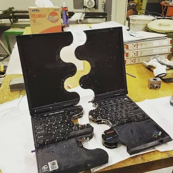 Laptop cut in half along a wavy line, its sliced keyboard sitting on a workbench.