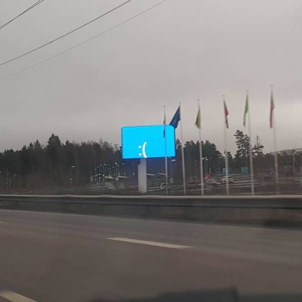 Roadside digital billboard showing a sad blue screen error face beside a row of flags.