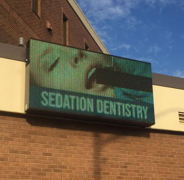Glitching LED sedation dentistry sign with a black bar across a patient's open mouth.