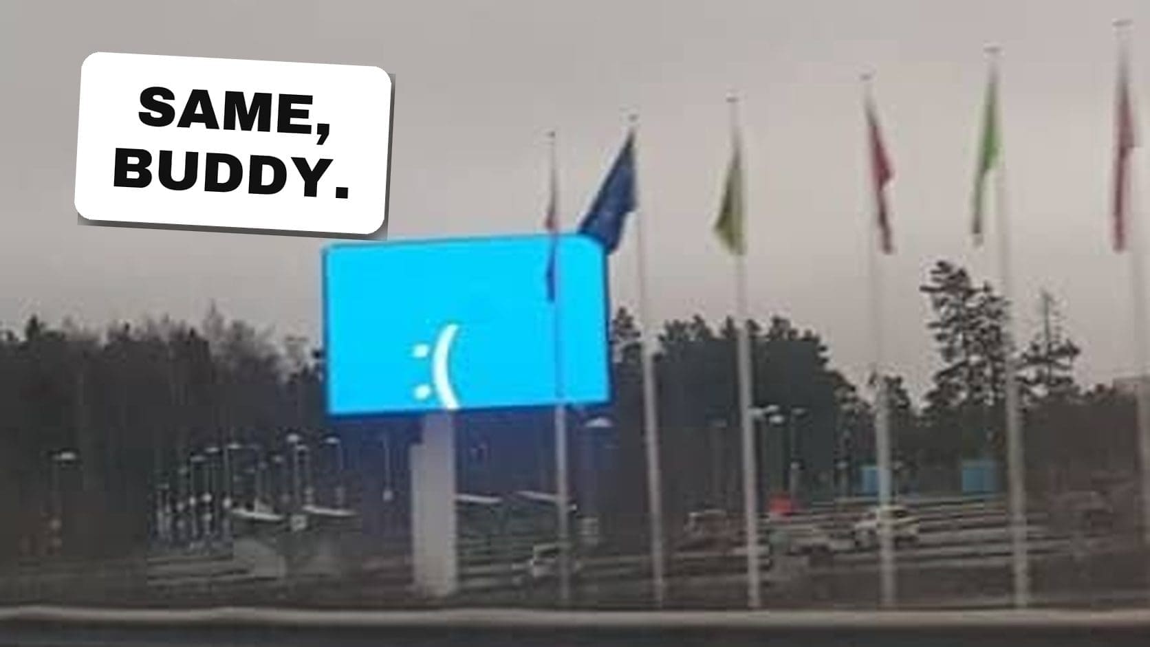Roadside digital billboard showing a sad blue screen error face beside a row of flags, one of the most public tech fails.