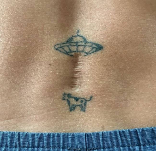 A unique tattoo featuring a UFO abducting a tiny cow using a scar as beam.