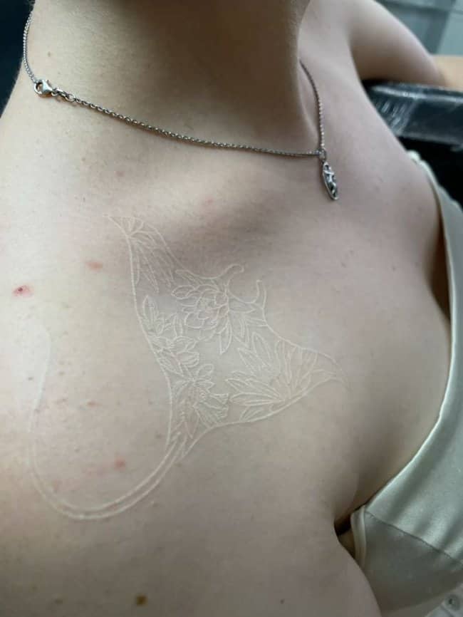 Intricate white ink manta ray unique tattoo filled with detailed floral botanical patterns on collarbone.