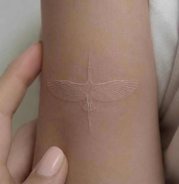 Subtle white ink crane bird in flight unique tattoo placed delicately on inner forearm.