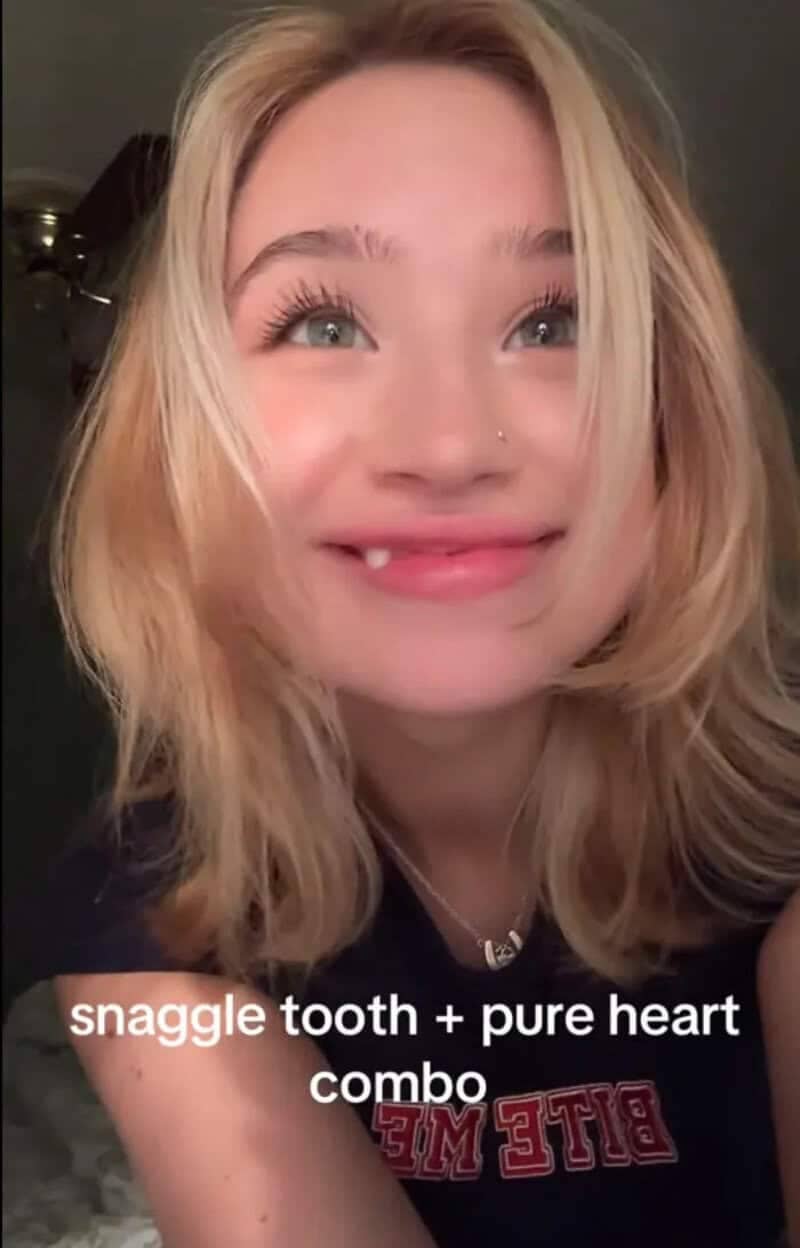 Smiling blonde girl showing off her prominent snaggletooth embracing facial wabi sabi features online.